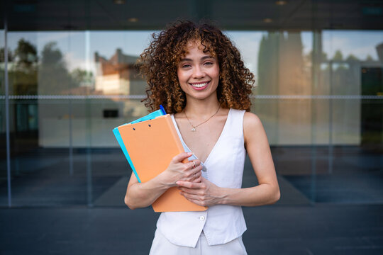 Professional business woman smiling holding folders with curly hair