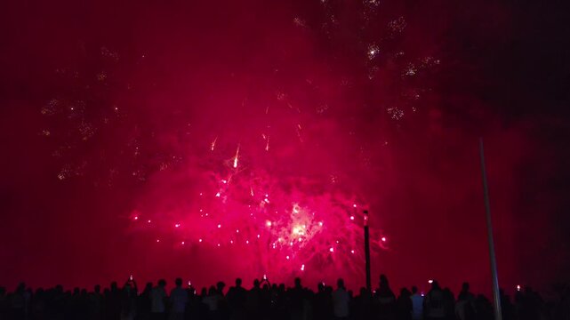 Red fireworks illuminate the night sky over Antibes as silhouetted spectators celebrate France's Bastille Day on the Riviera