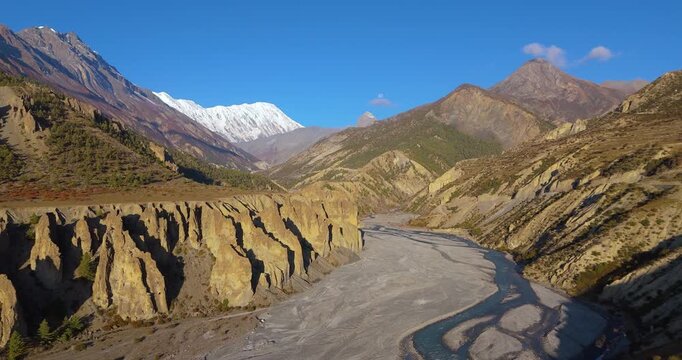 Annapurna Circuit, Manang region, Nepal, drone shot of eroded rock cliff formations along Marsyangdi River valley with snow-capped Tilicho peak mountains