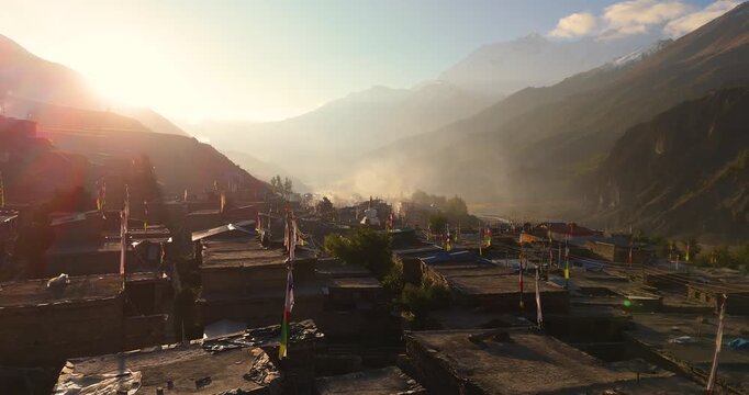 Drone shot of sunrise over a traditional Himalayan village shrouded in fog and haze along the rugged Annapurna Circuit, Manang Nepal.