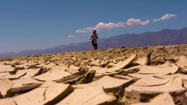 Wide shot of badwater marathon athlete running past dried up mud in death valley