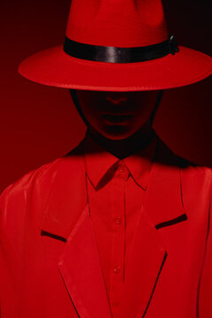 Person wearing vibrant red classic hat and matching sharp suit with black accents stands against red background. Fashion style portrait with strong creative lighting and shadows.
