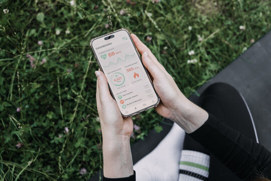 Woman sitting cross legged on mat looking at health dashboard on smartphone. Health data visualization, personalized health tracking, biometric data app, Data driven wellness