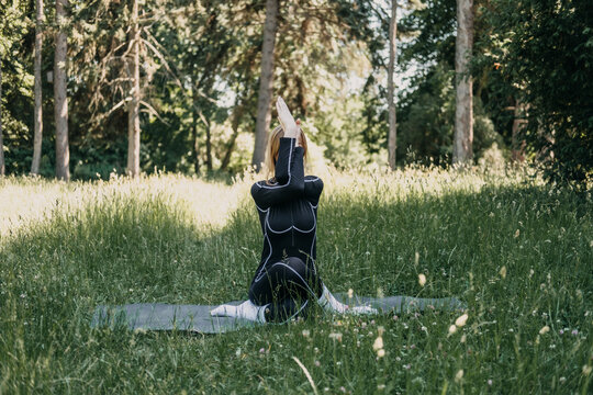 Woman practicing yoga in a grassy meadow surrounded by trees. Forest meditation, grounding exercises, stress relief techniques, mental clarity practice.