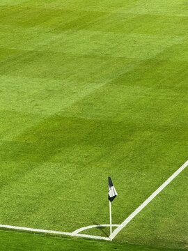 Close-up of a corner flag on a perfectly maintained lush green football pitch, vibrant grass, professional stadium, natural daylight, cinematic sports scene