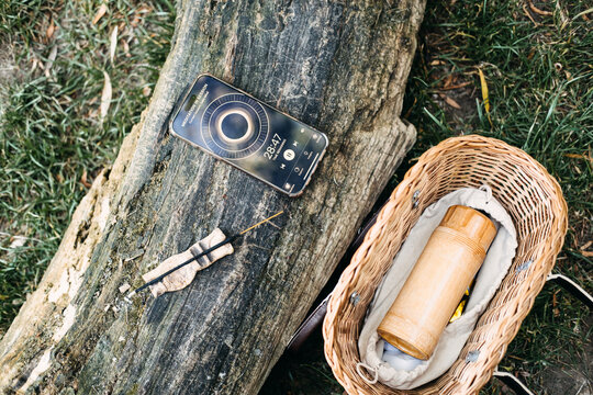 Smartphone showing screen sits on log beside burning incense and wicker basket. Meditation app screen, mindfulness app interface, guided meditation timer, meditation session tracker.