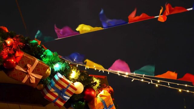 Festive Christmas market decorations at night, colorful bunting flags and glowing fairy lights, holiday gift boxes and evergreen garland