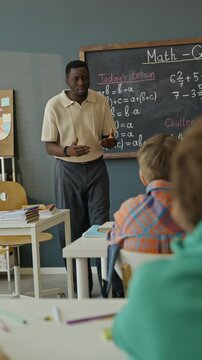 Vertical video of African American male teacher explaining math formulas on blackboard to multiethnic children. Footage is perfect for school advertisements and educational campaigns