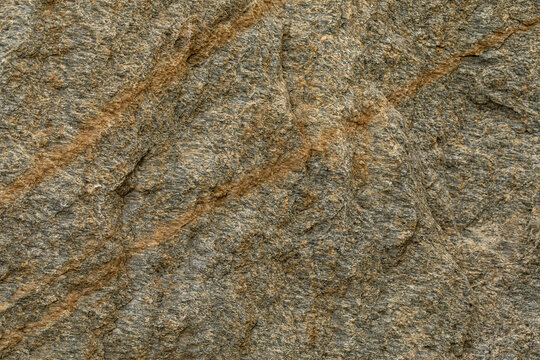 Natural raw rock surface with a weathered, tactile texture. Gray-brown gneiss stone features prominent diagonal brownish-orange mineral veining, creating a earthy, organic and durable backdrop.