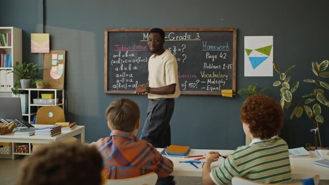 African American teacher explaining math lesson to diverse elementary school students in classroom. Footage is ideal for school promotional videos and educational marketing campaigns