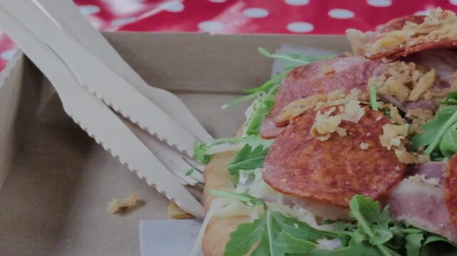 Close-up of a delicious Langos, a traditional Hungarian fried dough, loaded with various meats, fresh arugula, and crispy onions in a takeaway box. Street food culinary experience.
