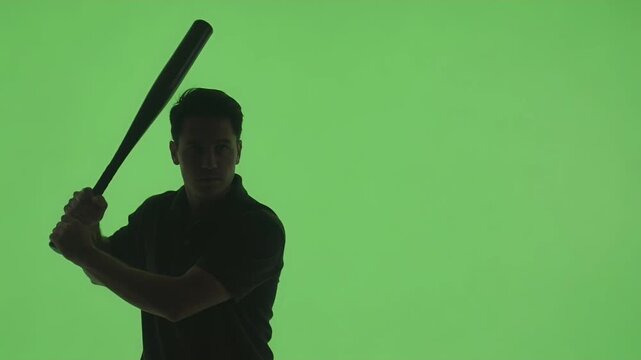 Baseball player silhouette stands ready to swing a bat against a solid green background for chroma key compositing.
