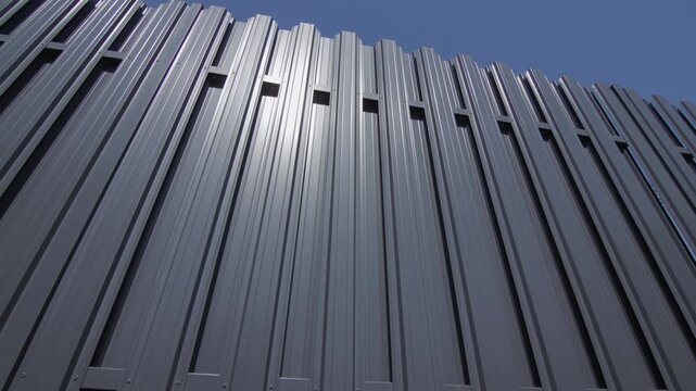 Modern architectural gray metal wall siding with corrugated texture under clear blue sky.