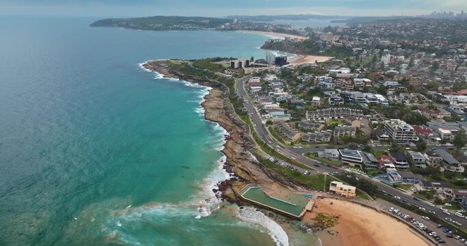 Sydney Manly Beach beautiful coastline ocean pool with rolling waves and residential building area, capturing summer vacation, travel, and leisure along the Australian shore. Aerial view drone flight