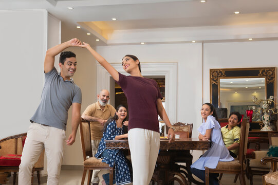 Young couple dance in the living room while the family watches