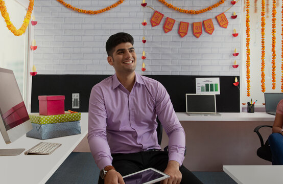 Happy man sitting on his desk  holding a tablet on the occasion of Diwali