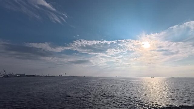 Cinematic real-time video of dramatic cloudscape over sea with sun glint and industrial skyline