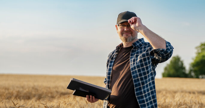 Middle aged male farmer holding a paper clipboard, smiling and looking at the camera while touching his cap