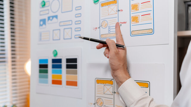Close-up of a UX designer reviewing wireframes, interface layouts, and visual design elements on a planning board for user interface development, usability testing, and digital product design.