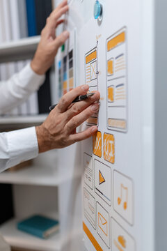 Close-up of a UX designer reviewing wireframes, interface layouts, and visual design elements on a planning board for user interface development, usability testing, and digital product design.