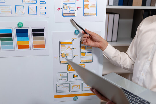 Close-up of a UX designer reviewing wireframes, interface layouts, and visual design elements on a planning board for user interface development, usability testing, and digital product design.
