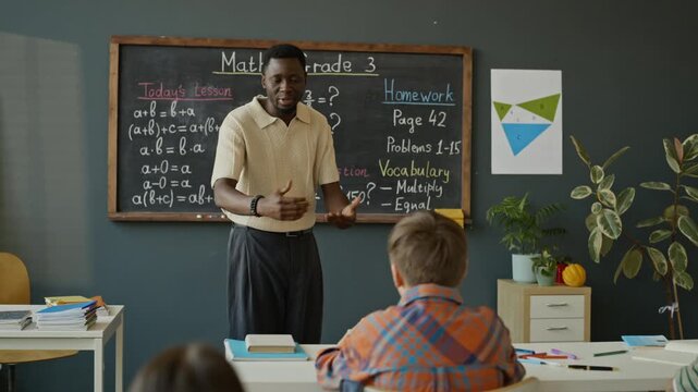 African American male teacher explaining math equations to diverse elementary school children in classroom. Clip is perfect for educational marketing and school promotional campaigns