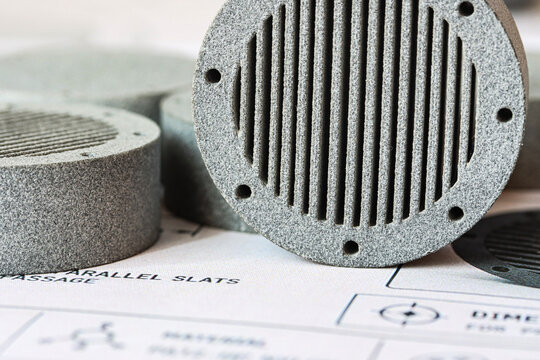Close-up of gray MJF 3D printed prototype parts placed on a technical drawing, showing rough nylon texture and additive manufacturing details for engineering, product design, rapid prototyping and ind