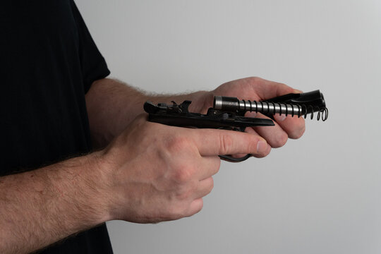 Close up of man hands disassembling semi automatic pistol by separating slide from frame with recoil spring on neutral background.