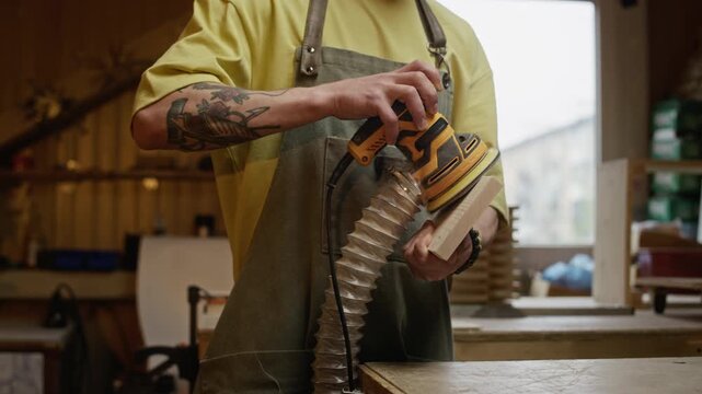 Caucasian young adult male carpenter using orbital sander on wooden block in workshop. Footage is ideal for promoting woodworking courses, small craft businesses, and power tool advertisements