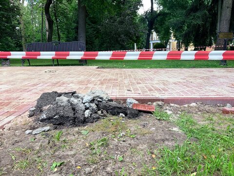 Repair work in the city. a pile of excavated dark soil, rocks, and broken red paving bricks on the ground next to a newly laid brick pathway.