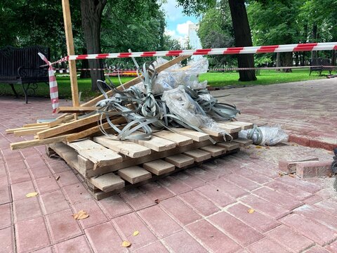 Pile of construction waste on a wooden pallet cordoned off by red and white barrier tape in a park. City repair