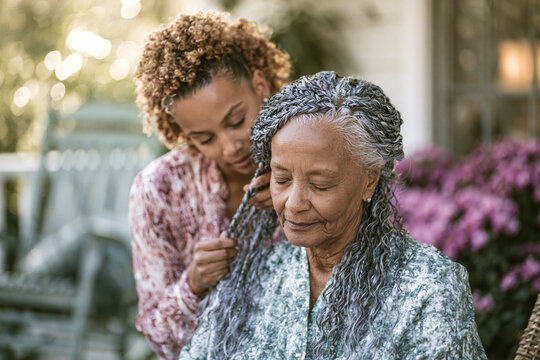 Granddaughter braiding grandmother's hair on porch