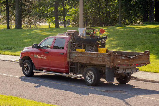Montreal, Quebec, Canada. July 30, 2026. Red municipal maintenance pickup truck carrying landscaping tools parked by a grassy park.