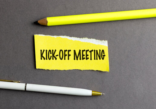 Kick-off meeting text on torn paper with pencil and pen on gray background
