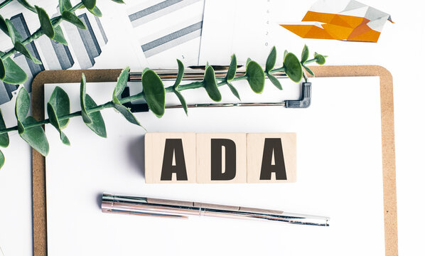 Ada acronym spelled with wooden blocks on clipboard with financial charts, pen and green leaves on white background