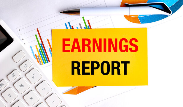 Earnings report text on yellow card with calculator, pen and financial charts on office desk
