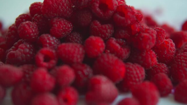 Fresh organic raspberries falling in slow motion on a white background, creating a delicious and healthy fruit pile