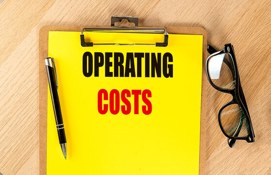 Operating costs text on clipboard with pen and eyeglasses on wooden background