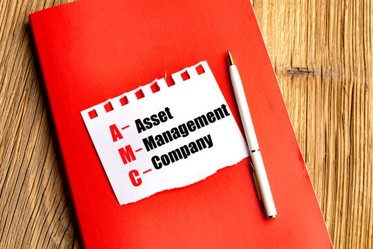 Asset management company acronym amc written on torn paper with pen and red notebook on wooden background