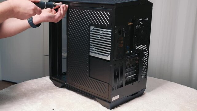 Removing side panel from computer case during assembly, unscrewing and removing the side cover with a screwdriver on a work surface during personal computer build