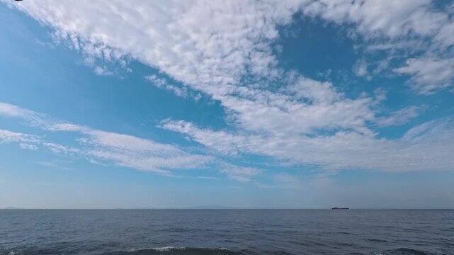 Cinematic real-time video of dynamic cloudscape and blue sky over tranquil ocean horizon with ship