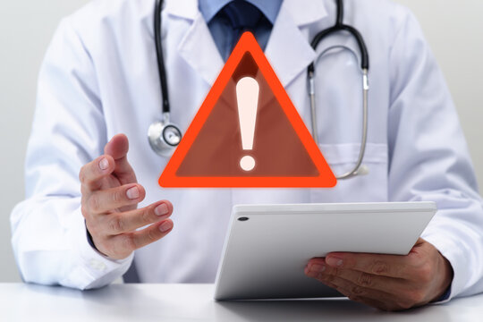 Doctor warning patient about potential health risks during medical consultation. Physician using digital tablet. Red triangle warning icon.