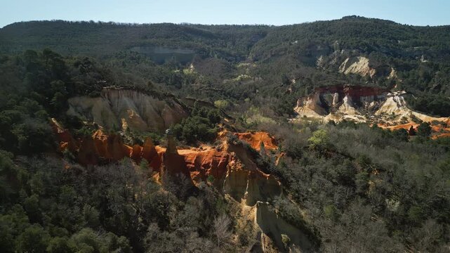 A drone shot of the sprawling ochre cliffs of Rustrel in France. The tall red cliffs rise high above the trees and stretch across the forested landscape.