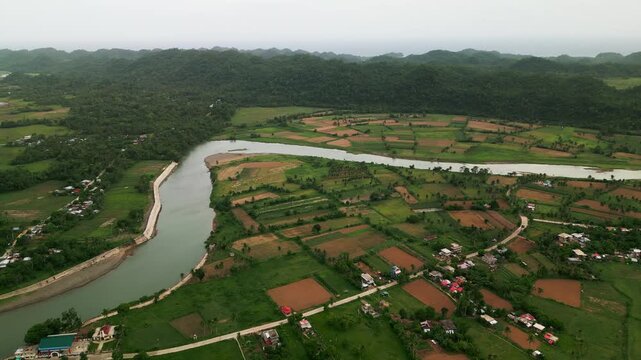 Panoramic aerial overview of a winding river, patchwork farmlands, scattered homes, and lush tropical hills - Pajo, Virac, Catanduanes, Philippines