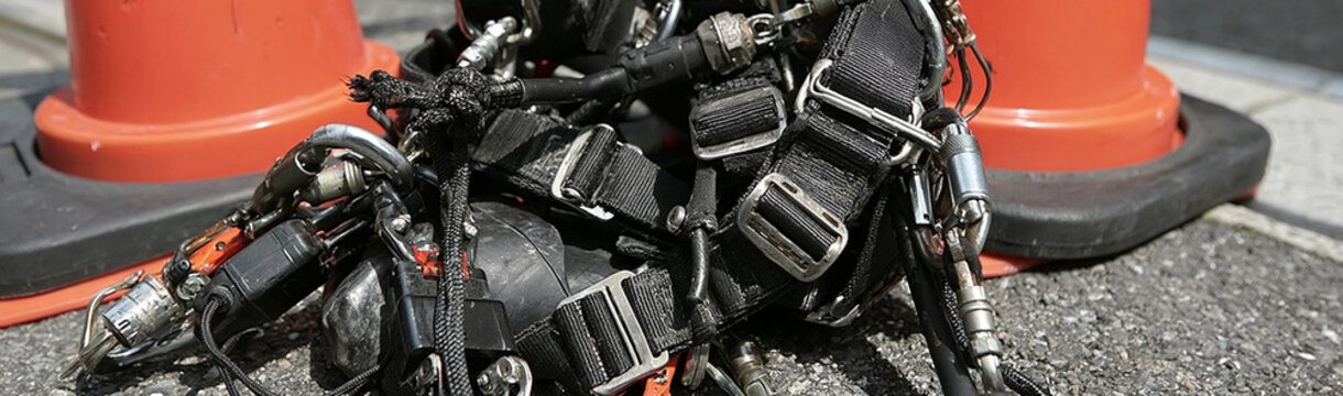 Diving Gear on Pavement: A close-up view of tangled diving equipment, including a harness and other accessories, resting on a rough, paved surface next to orange traffic cones.