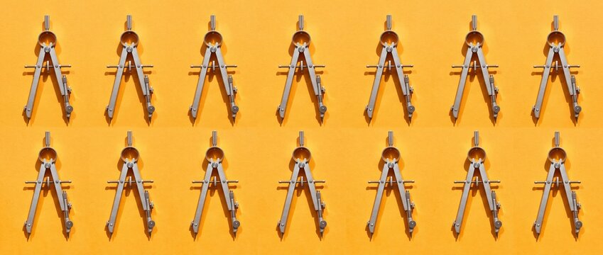 A uniform grid of metal drawing compasses creates a repeating pattern, casting distinct shadows on a bright orange background