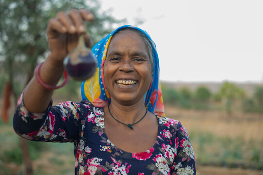 woman holding brinjal and smiling,in the field 