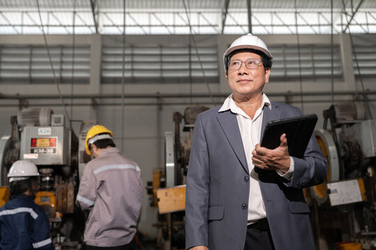 Senior Asian man in hard hat and suit standing in industrial factory