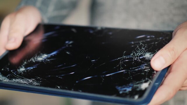 Close up of hands holding tablet with broken cracked screen display in slow motion.