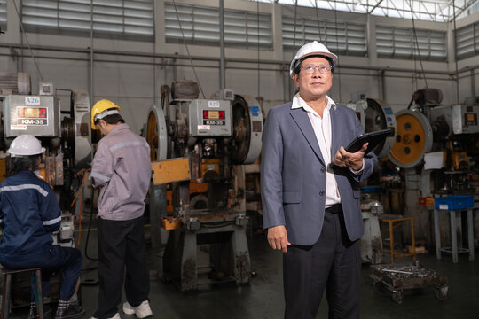 Senior Asian man in hard hat and suit standing in industrial factory